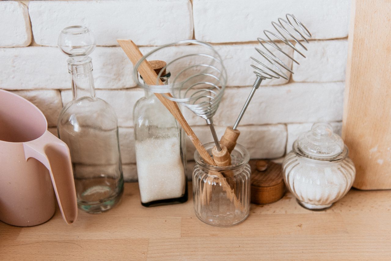 The Art of Drawing Readers In: Your attractive post title goes here A collection of glass jars and kitchen utensils on a rustic wooden counter with a white brick background.