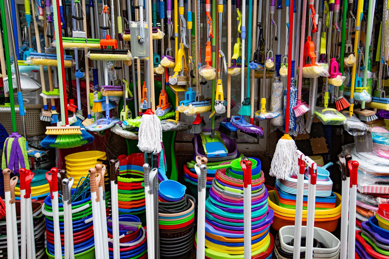 contact-img Various colorful mops and brushes arranged with stack of plastic basins and bins in household goods supermarket